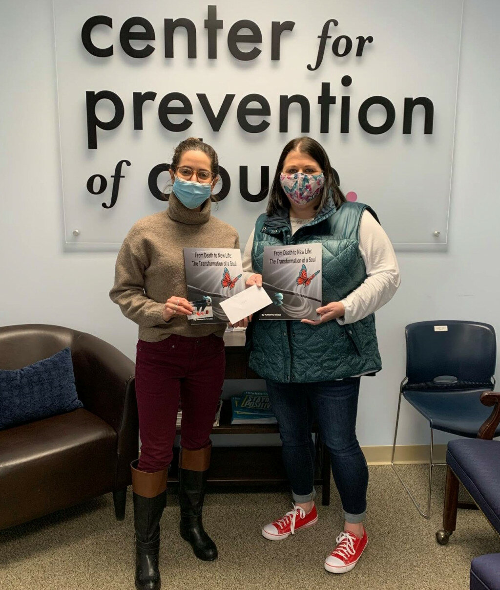 Kimberly Souba, right, donates two copies of her book and the first proceeds check to Camille Yameen, Director of Marketing and Communications for the Center for Prevention of Abuse. (Photo contributed)