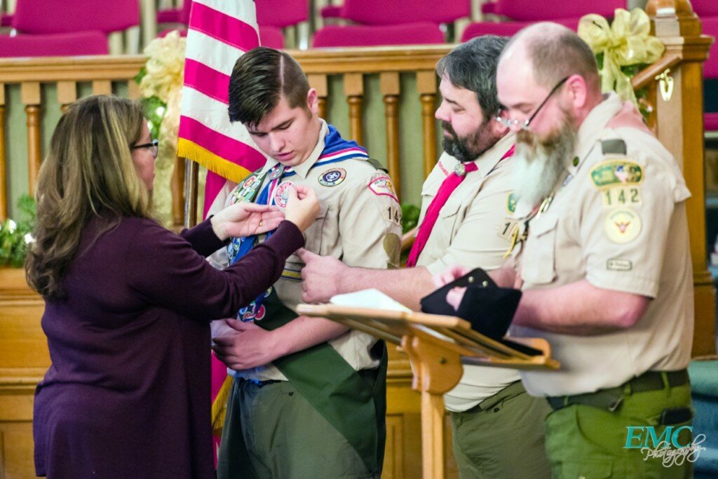 Courtesy of Ed Cicenas — 
Kathy Drozs places the Eagle Patch on her son, Zach’s, uniform during the Court of Honor help at the Clinton Presbyterian Church as his father, Chris, help. Scoutmaster Ron Armstrong, far right, tell the people gathered about the achievement.