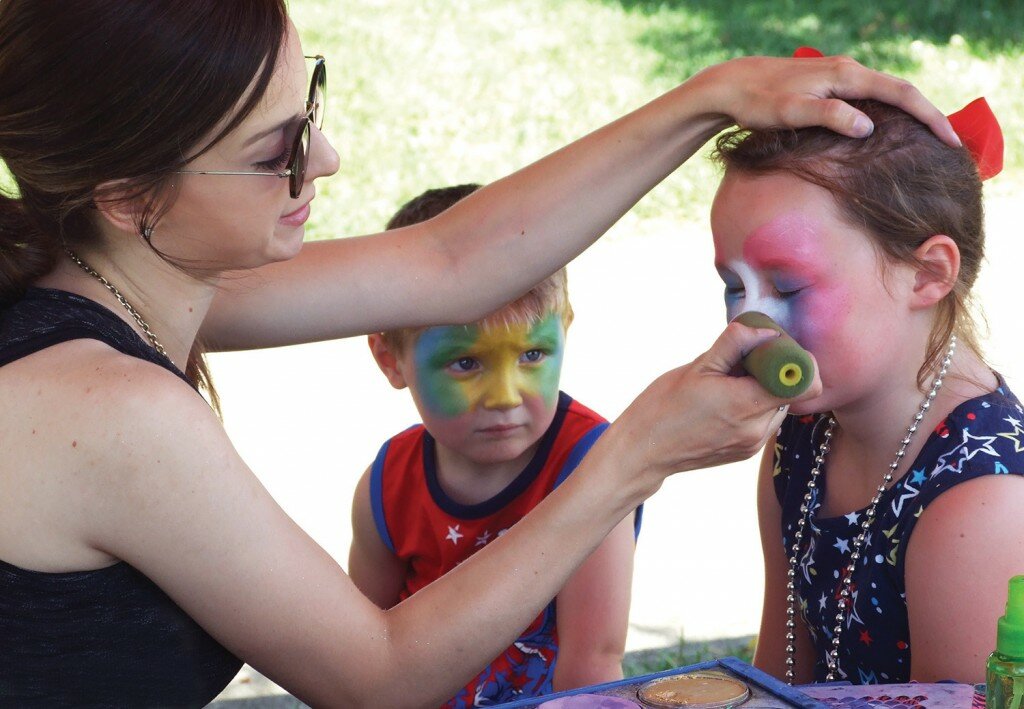 Gordon Woods / Journal — A helper for the Zoo Lady painted faces July 4 as families had a good time on Mr. Lincoln's Square celebrating Independence Day with help from Celebrate Clinton.  Food, a watermelon-eating contest, dunk tank and entertainment were among the activities.