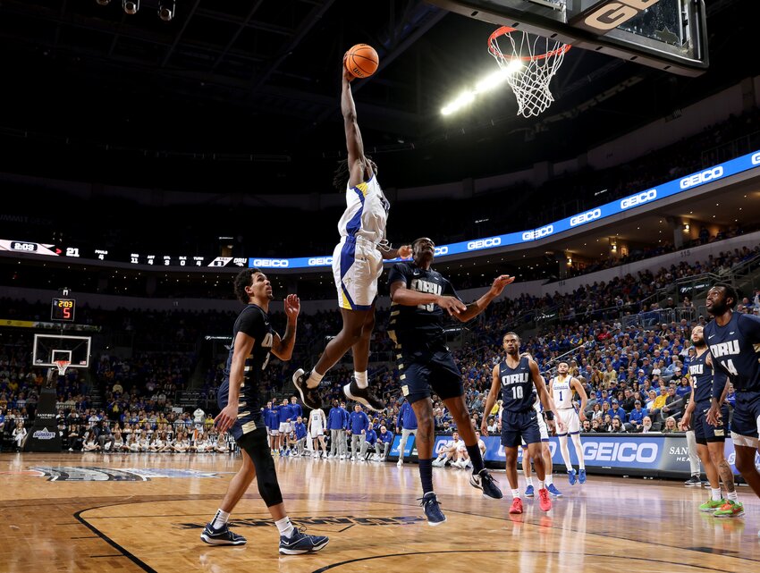 William Kyle III (#42) of the South Dakota State Jackrabbits leaps to slam dunk the ball over Sir Issac Herron (#23) of the Oral Roberts Golden Eagles at the 2024 Summit League Basketball Championship at the Denny Sanford Premier Center in Sioux Falls.