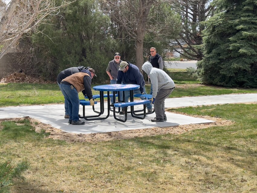 A handful of city employees place the new picnic table, which was purchased through the Torrington Rotary Club, in its new location on the walking path while Bob Taylor and Tim Pieper anxiously await the final result.