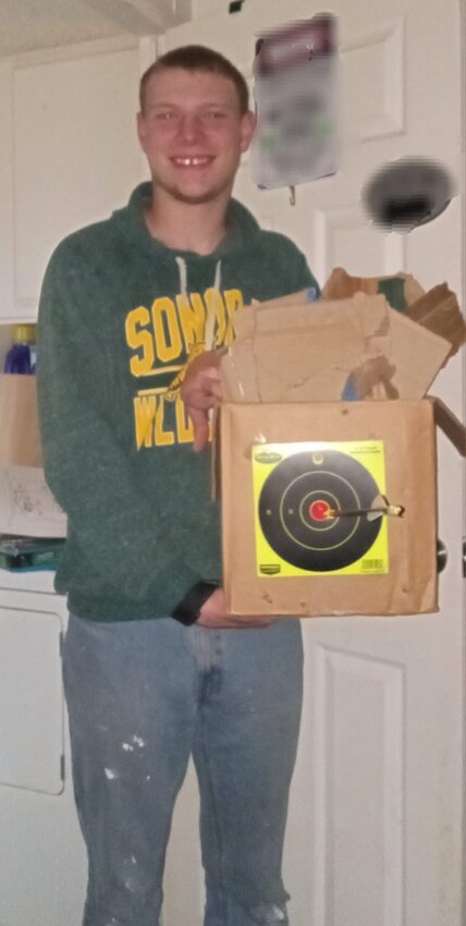 Rowan Littauer, charged with first-degree murder for shooting Dakota Farley in the chest with a compound bow and two broad-head arrows, is pictured holding a cardboard box that’s filled with broken-down pieces of more cardboard. A bull’s-eye is taped to the front of the box and a black arrow pierces its center. The caption on the April 2024 photo posted to Leah Leisure's Facebook page reads, ‘Great shot Rowan!’
The blurred-out sign behind him reads, 'WARNING BEHIND THIS DOOR I MAY OR MAY NOT BE GETTING HIGH ENTER AT YOUR OWN RISK.'