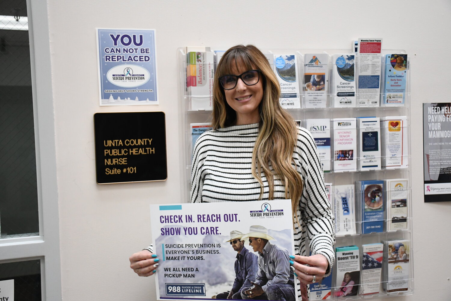 Uinta County Community Prevention Specialist Kendra Safford presents one of her program’s Pick Up Man suicide prevention campaign posters in front of Uinta County Public Health at the Human Services Building in Evanston, where she can be reached in person or by phone at 307-789-9203 ext. 212.