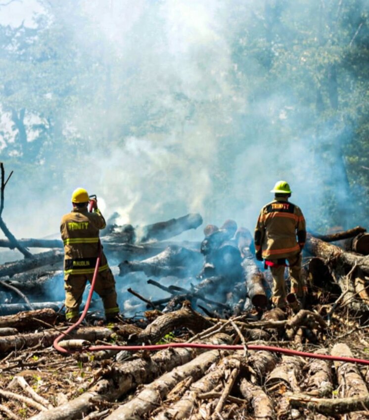 Firefighters from Trinity and Friday fire departments work to extinguish a fire on stacks of lumber on Sunday.
