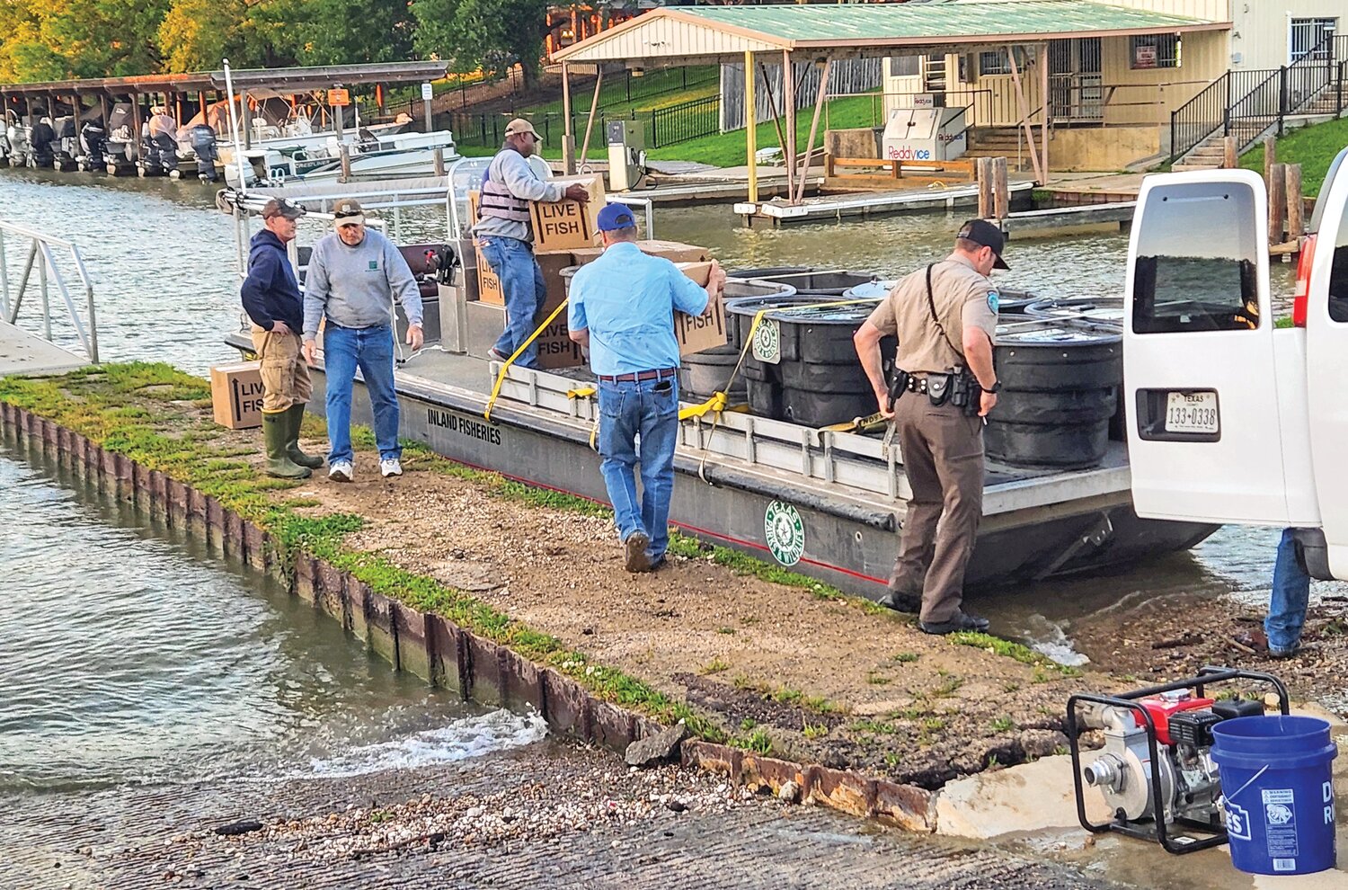 Lake Livingston Project Manager Chad Holton (in blue shirt and blue cap) carries a box of fry to the fish-stocking barge. Each box contains 50,000 fry. Photo by Emily Banks Wooten.