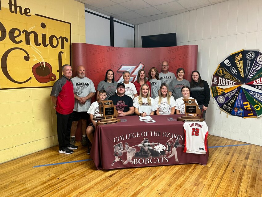 As Allyssa Joyner signed her National Letter of Intent with College of the Ozarks, she was joined by family and coaches. At the table, from left: Joyner&rsquo;s brother Avery, father Jason, Allyssa, mother Michelle, and sister Adilee. Standing: Lady Zizzers Head Coach Scott Womack, grandpa Allen Joyner, Aunt Virginia Uphaus, Grandma Kathy Joyner, Bobcats Coach Becky Mills, Grandma Jodie Haynes, Grandpa Donnie Haynes, Lady Zizzers assistant coach Sammi Rodosevich, and Lady Zizzers assistant coach Hailee Erickson.