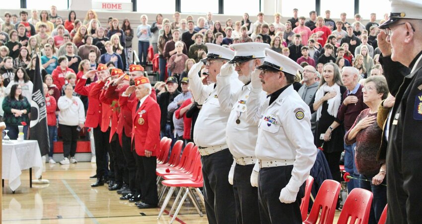 Local veterans, including a group of Marines at left, salute the American flag during the singing of the 