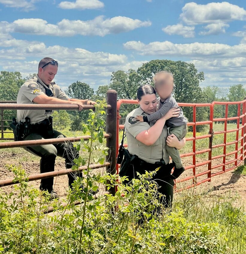Deputy Tessa Jens carries a 2-year-old child to safety Friday afternoon as Deputy Jacob Hamby climbs a fence to get out of a field in which he found the toddler, just west of the child&rsquo;s home. Deputies were called to help look for the child by the toddler&rsquo;s mother after she and others searched unsuccessfully for 10 minutes.