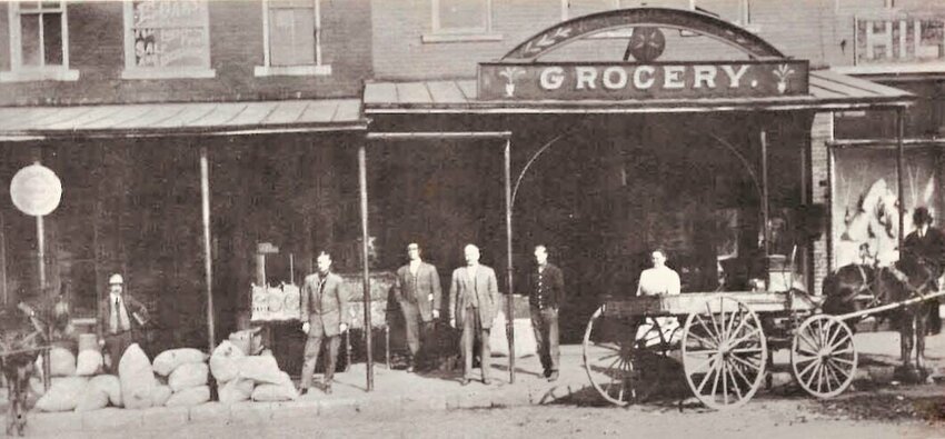 The exterior of the Star Grocery circa 1910. The two gentlemen at the center of the photo are Captain Mark and Judge W.A. Springer. The woman is Elsie Springer. One of the other men is George Wiggins.