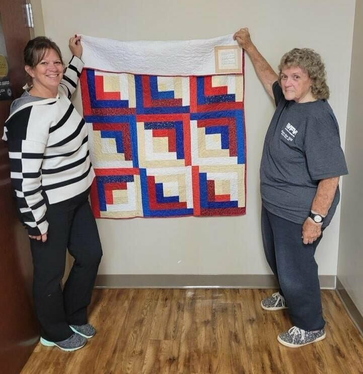 A quilt made by veteran Brenda Parker was donated to the West Plains Veterans of Foreign Wars Post 1828 Auxiliary member Freeda Evans, right, who then gave it to Julie Weaver, a veteran and a counselor for the U.S. Department of Veterans Affairs clinic in West Plains, left, in appreciation for her years of service and assistance to veterans. The quilt is a patriotic-themed log cabin design in a red, white and blue color scheme with stars.