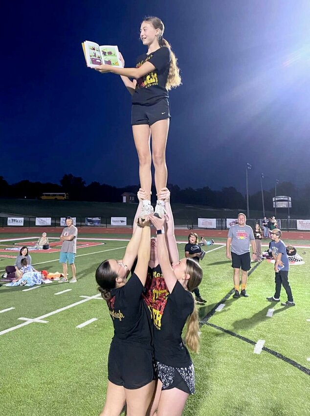 Cheerleaders Kayleigh Kinder, left, Myleigh Berry, center, and Shaley Francis, right, hoist teammate Kennedi Wooderson as she reads to a captive audience including Nathan Huddleston and his sons, at right, during West Plains High School’s “Under the Lights” event held Oct. 3 at Zizzer Stadium. At left are Emily Edwards-Long with her daughter Layla Long and Cash Young on the blanket, and Cash’s dad Kevin Young standing. Students in grades kindergarten through six enjoyed an evening filled with reading with their families and teachers, hot dogs, finger lights and glow bands. Several high school athletic groups read to the youngsters, including members of the football team. “It was a wonderful opportunity to foster a love for books and celebrate our commitment to reading in the West Plains School District,” said district Communications Director Lana Snodgras. “Thank you to everyone who joined us.”