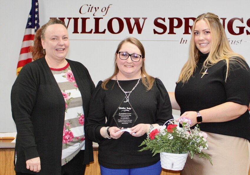 WILLOW SPRINGS &mdash; Willow Springs City Clerk Heather Tooley, center, was recognized Thursday evening during the Willow Springs City Council meeting for earning her Missouri Registered City Clerks designation. It is to be formally awarded March 12 in Columbia at the annual Missouri City Clerks and Finance Officers Association Spring Institute. The association&rsquo;s South Central Director and Ava City Clerk Suzanne Welsh, left, and South Central Secretary and West Plains City Clerk Kellie Mayers, at right, presented Tooley with a plaque and flowers thanking her for her dedication, leadership and hard work.
