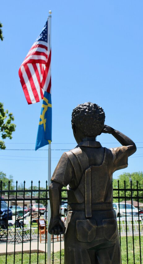 Standing frozen in a gesture of respect, pride and patriotism, the subject of a recently unveiled bronze statue at Lincoln School, “I too, am America,” expresses the determination of pre-segregation-era Black Americans to participate in and contribute to the ideals of democracy. The pedestal was painted with an American flag and portraits of civil rights leaders and notable Black Americans by muralist Dr. Bolaji Ogunwo, whose work can be seen in other public spaces throughout West Plains. It is one of two statues on the Lincoln School Reflection Plaza, dedicated in a ceremony held May 17.