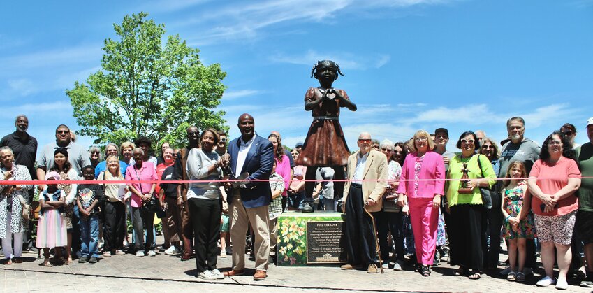The Lincoln School Reflection Plaza dedication ceremony was held May 17, attended by dozens of community members, government officials, and community members who have contributed to the school’s restoration and promotion of Black history in West Plains. Presentations were made thanking those who devoted time, talent, effort and financial support, and concluded with a ribbon cutting ceremony coordinated by the Greater West Plains Area Chamber of Commerce to officially introduce the park to the public. Two bronze sculptures of Black children, one with a theme of patriotism and resilience and the other with love and courage have been installed on the grounds of the restored historical Black schoolhouse, surrounded by landscaping and seating. The restoration of the school has been led by Crockett and Tonya Oaks III, holding the ribbon-cutting scissors, as the Lincoln School Project. The couple have also coordinated other efforts to honor the memories and history of Black community members and their contributions to West Plains during an era of inequality and segregation. In the words of Tonya Oaks, whose likeness as a child is the model for the statue of a girl making the “heart” symbol with her hands, “Change doesn’t begin with policies or laws, it begins with people.”