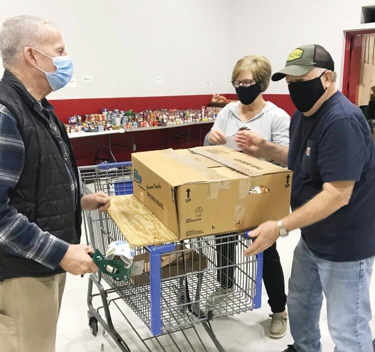 Working as a team, Ralph Crampton, Pam Irwin and Danny Irwin fill food baskets for McClain County Operation Christmas.