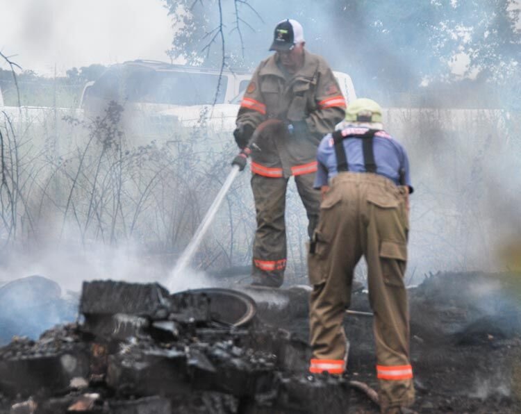 Two firefighters stand on smouldering rubble as they extinguish hot spots in a junk yard fire north of Lexington on Tuesday.
