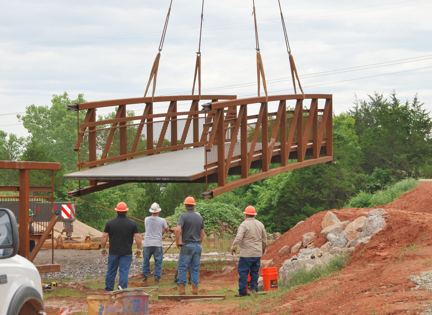 The new walking bridge over the spillway at the Purcell City Lake was put together and set last Friday morning. Utilizing a huge crane, crews had to insert the protruding iron arms into receiving ones and then bolt the two sections together. The bridge is 120 feet long. Designed and manufactured by Contech Engineered Solutions LLC at a cost of $191,000.