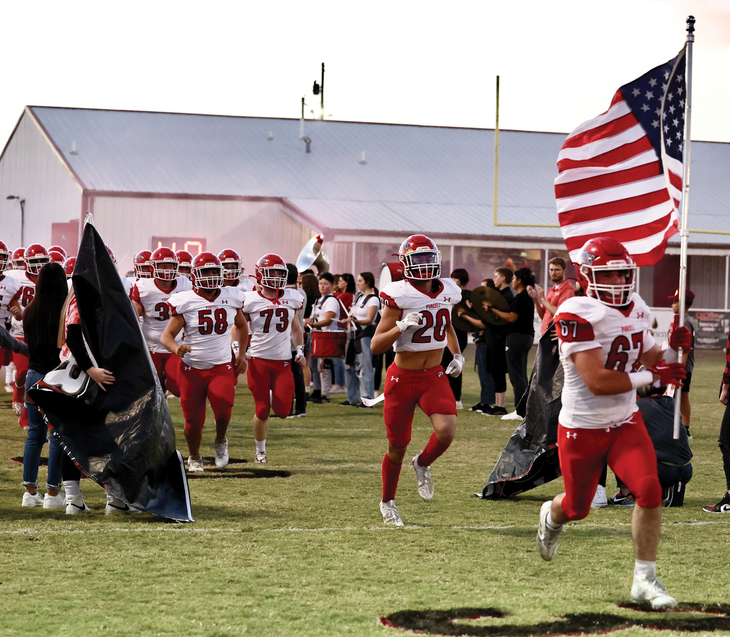Purcell senior Luke Edelman (67) leads his team on the field in Washington carrying the American flag last Friday night. The Dragons fell to the Warriors 40-7.