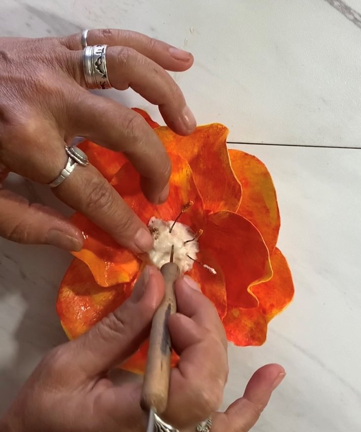 Create the center of the flower out of fondant. Attach to petals. Shape with cake tool. Press the prefabricated stamens into the center. ..