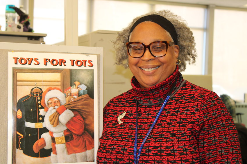 Thelma McIver stands in front of a Toys for Tots box.  She is head social worker examiner and assistant to Giselle Steketee.