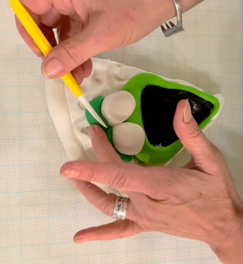 Roll green fondant into two small cylinders for eyebrows. Attach eyeballs to face with corn syrup...