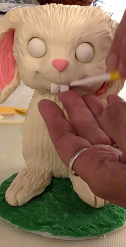 Shape ears out of fondant and attach to head. Roll two balls of fondant for eyes and add to socket. Sculpt nose out of fondant of your choice and add to face. Do the same for bucked teeth. Roll another ball of fondant and attach to backside for a cotton tail.