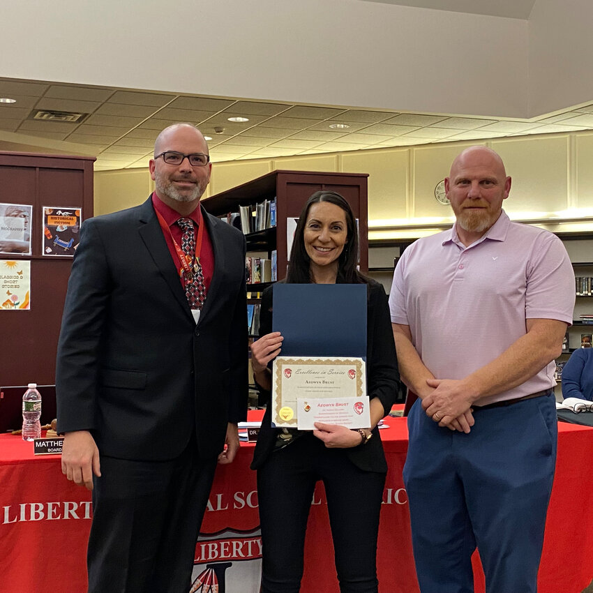 Excellence in Service Award winner Aeowyn Brust poses with Superintendent Dr. Patrick Sullivan, left and Board President Matthew DeWitt, right.