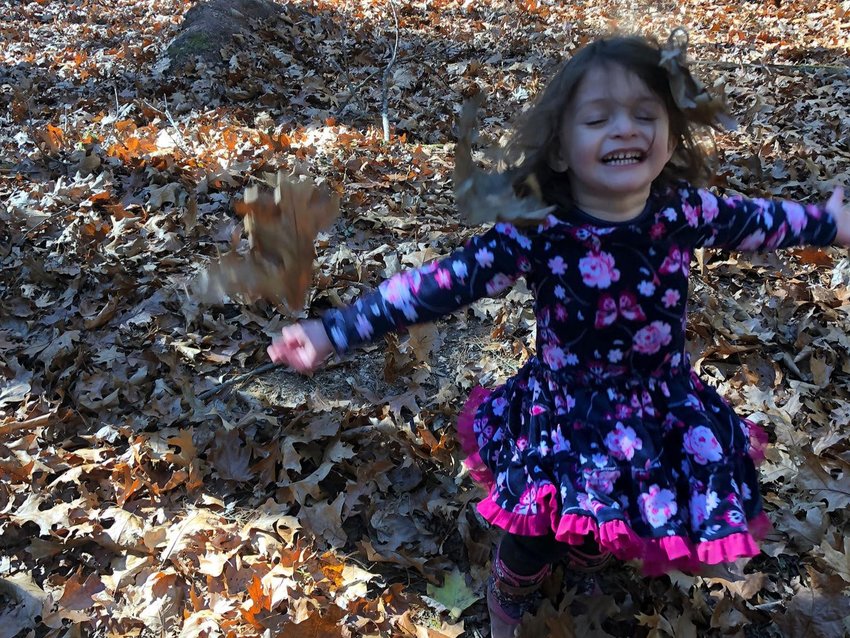 A three-year-old plays in the leaves, radiating joy.
