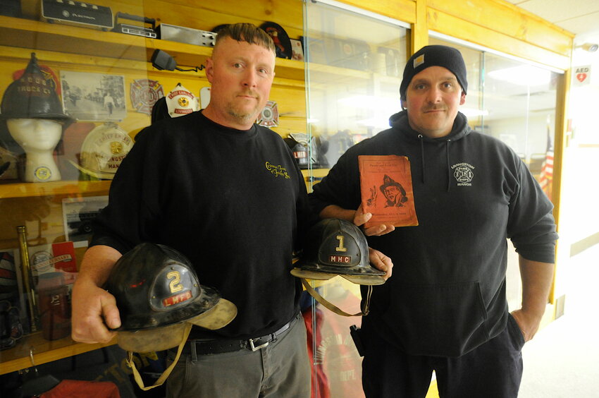 Proud of their heritage. Lt. Charlie Hoag, left, and Chief Robert Trotti, Jr., right, joined the local volunteer fire department as teenagers in 1999. Over the years, they have been instrumental in collecting and preserving historical artifacts related to the department. Hoag is pictured holding original firefighter&rsquo;s helmets from Hoos Truck Company and Manor Hose Co #1, while Trotti is showing off an extremely rare brochure from the first SCVFA parade, which was hosted by Manor on Wednesday, October 3, 1928.