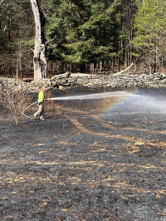 Kauneonga Lake and White Lake firefighters spray down a fast-moving brush fire earlier this month that reduced a field of dry grass to ash.