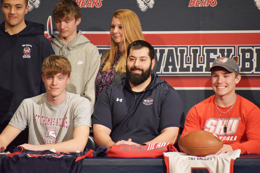 Talan Scanna (left) and Austin Hartman (right) pose alongside Coach Kevin Crudele (center) as well as their families after signing letters of intent to play college football.