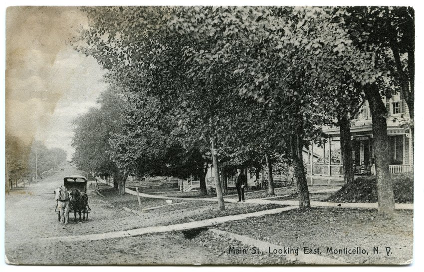 'Main Street' looking east: The Republican Watchman reported in 1908 that Monticello village trustees had decided to change several street names, including renaming Main Street to Broadway, and discontinuing the use of &ldquo;East&rdquo; and &ldquo;West&rdquo; along its route. This postcard mailed in 1908 shows The Osborn, a boarding house operated by the Osborn sisters, which was later demolished. The hotel was located on the south side of the street, across from the intersection of Jefferson Street with Broadway. Note the wooden bridge that spans the distance between the curb and the sidewalk, offering pedestrians a place to alight from a carriage without stepping into mud and other debris. Broadway was first paved in 1912.
