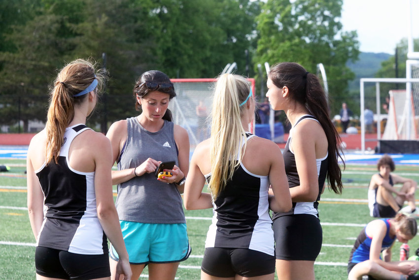 Sullivan West girls track coach Skylar Musa checks some data on her phone to advise runners Grace Boyd, left, Abby Parucki and Samantha Everett during the Section Nine Track and Field Championships staged at Rondout Valley. The Lady Bulldogs captured the title, which was the sixth one in the past seven years.