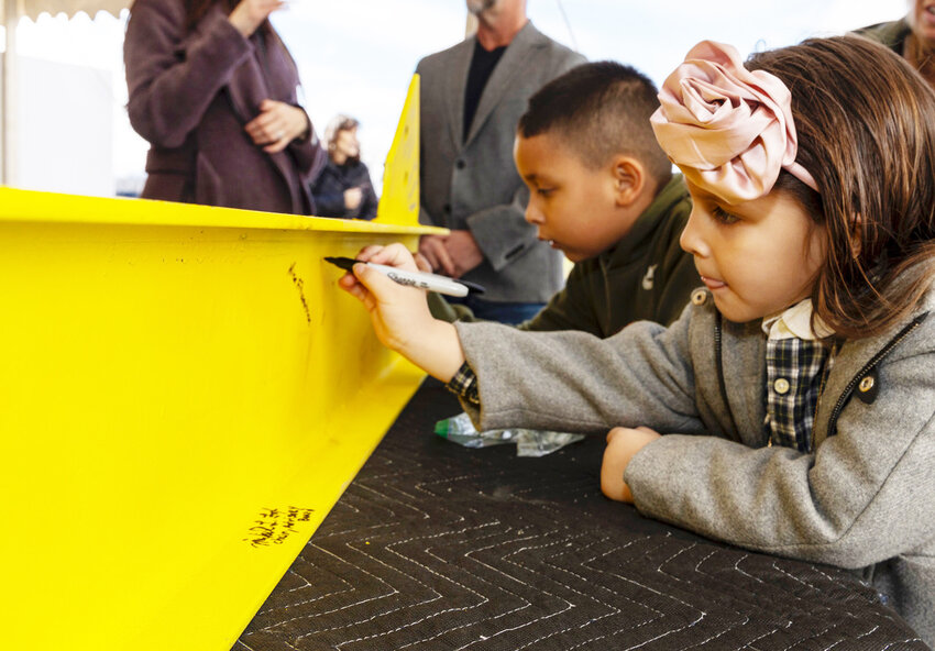 Children signing a symbolic yellow steel bar for display.
