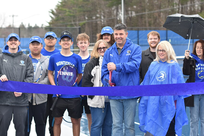 The Monticello Athletic Director, tennis team, and members of the school board gather together to cut the ribbon to open the new tennis courts.