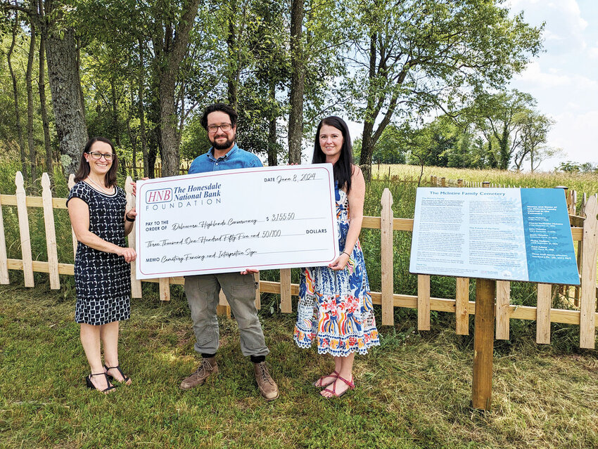 Pictured, from left, are Elizabeth Nagy, Honesdale National Bank Foundation; and Lucas Green and Samantha Mango, Delaware Highlands Conservancy, in front of the newly rebuilt perimeter fence and interpretive sign at the historic family cemetery on the Van Scott Nature Reserve property, Beach Lake, PA.