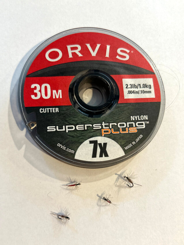 A cluster of tiny midge flies and a spool of 7X tippet, as fine as a human hair. (The spool of tippet is about 4 inches in diameter).
