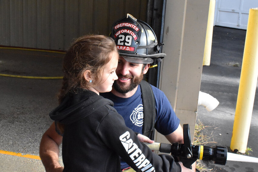 Firefighter Niko Niforatos smiles as his daughter Lucy aces the “fire extinguishing” station, where students spray water on a piece of wood painted to look like a fire.