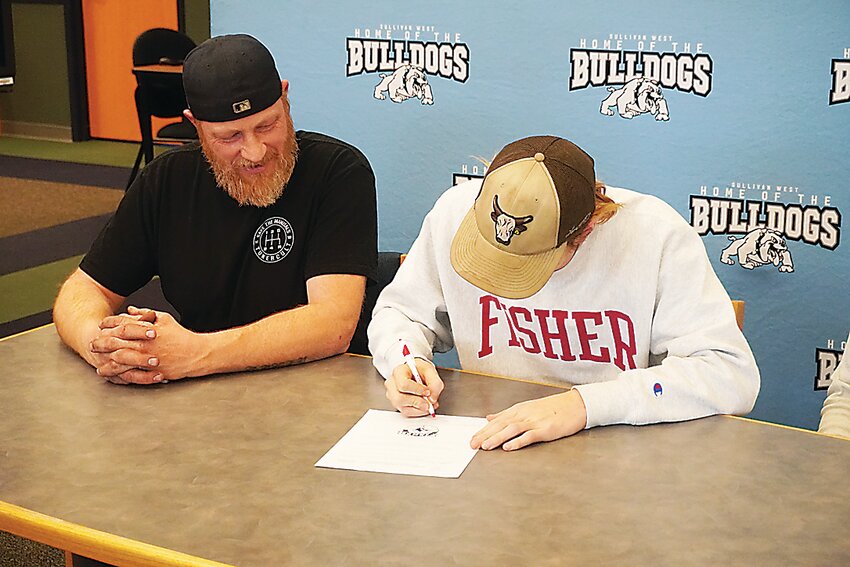 Adam signing his college letter as his dad Jeremy looks on.