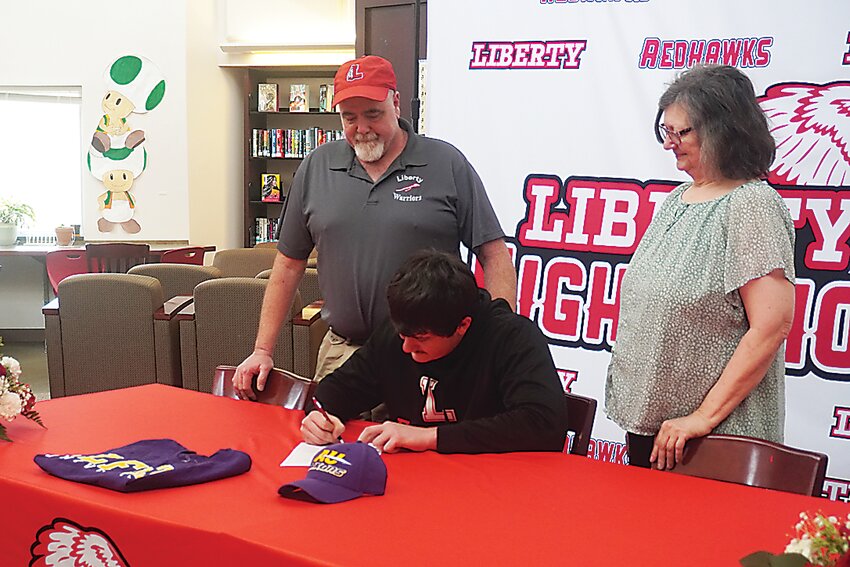 Matthew Lutz, signing his commitment letter to play football at Alfred University while his parents look on.