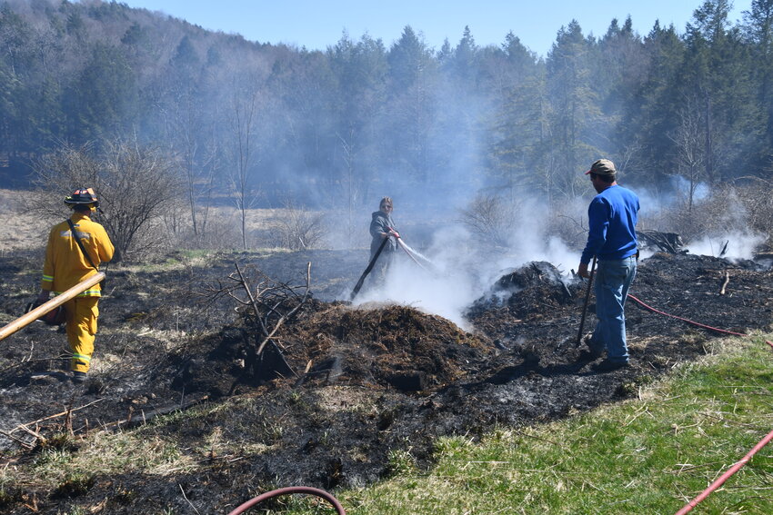 Nearly three dozen firemen from four fire companies worked on extinguishing the brush fire which claimed nearly five acres of land on Thursday afternoon in Galilee, PA. Above, Hortonville fireman Eric Dnistrian, left, carries in a chainsaw to fell two trees which were burning while Equinunk fireman Kylie Chrisler, center, hoses down a hot spot.