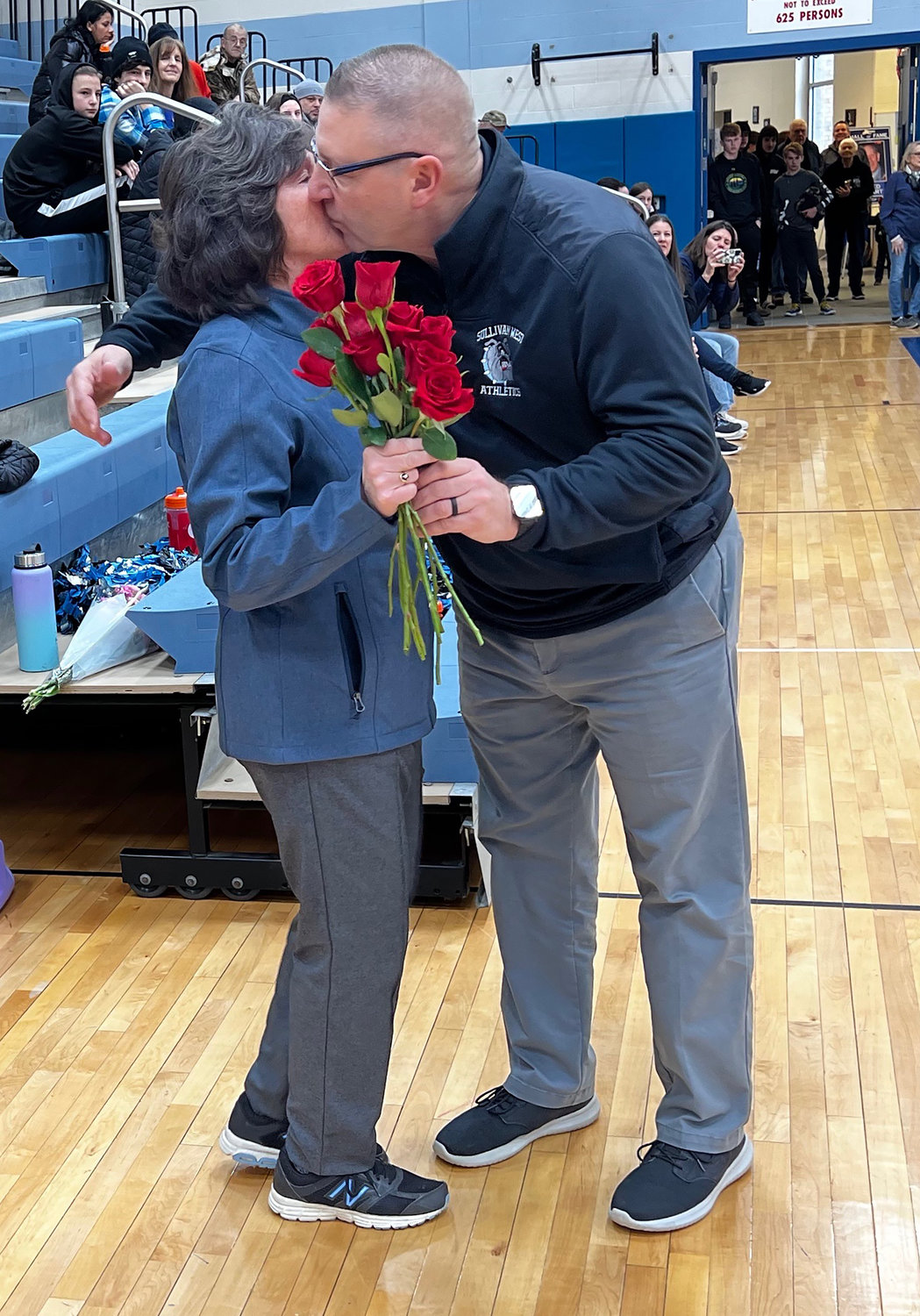 Sullivan West boys basketball coach John Meyer gives Becky Ahart a hug along with flowers prior to the game versus Monticello. Meyer, along with Roscoe/LM Athletic Director David Eggleton, Monticello boys basketball coach Chris Russo and Sullivan West Assistant Basketball Coach Jerry Davitt spoke glowingly about Fred Ahart and the remarkable influence he had on so many during his illustrious career.