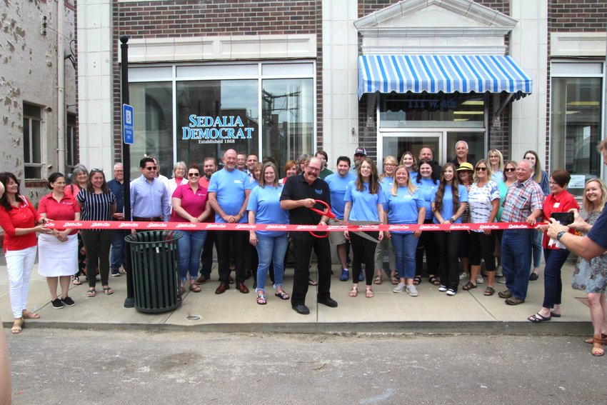Surrounded by community members, elected officials and employees, Sedalia Democrat Publisher Jim Perry cuts the ribbon celebrating the Sedalia Democrat&rsquo;s new location at 111 W. Fourth St. during an open house hosted Friday, June 10. The new building, formerly the Sedalia Water Department, is across the street from one of the Democrat&rsquo;s past locations at 108-110 W. Fourth St.