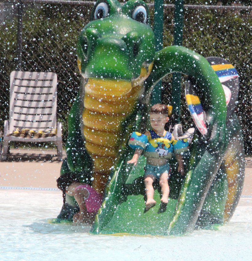 A kid slides down the dinosaur slide at Liberty Park pool on Friday as water from sprayers showers down on the children&rsquo;s area of the pool.