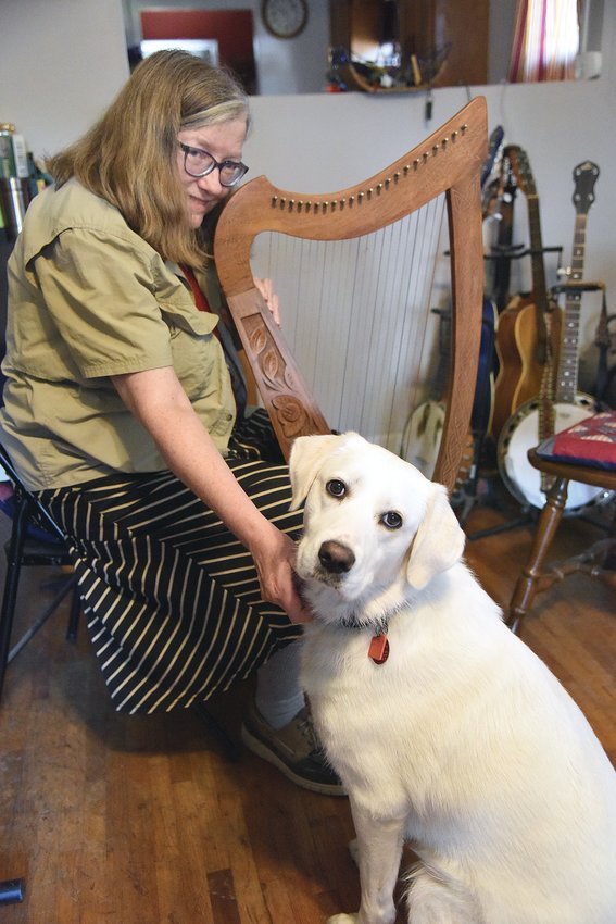 Artist and musician Linda Huber holds a Celtic, or lap harp, as she sits beside her dog Estelle Stella Luna on Thursday. Huber and her husband, Don Huber, moved to Sedalia 11 months ago. She recently participated in the NoBro Art Walk with her artwork and will perform as a musician for the event on Aug. 6.
