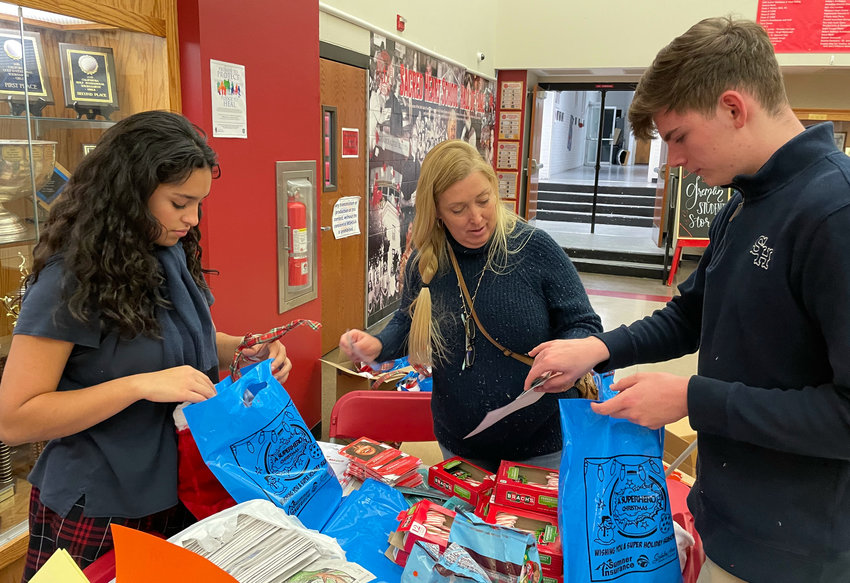 Sacred Heart Junior Xemina Lopez, Mykel Schlotterbeck with the Military Affairs Committee, and Sacred Heart Key Club member Stephen Belles stuff stockings Tuesday in the Sacred Heart Commons.