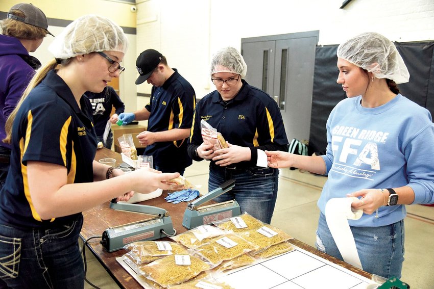 Green Ridge FFA members, from left, Secretary Macy Reed, Vice President Mattilyn Mergen, and Kayley Goodman help label pasta during Packing for a Purpose on Tuesday morning, Feb. 28 in the Smithton R-VI School multipurpose building. Pettis County FFA students gathered to pack meals for those in need.