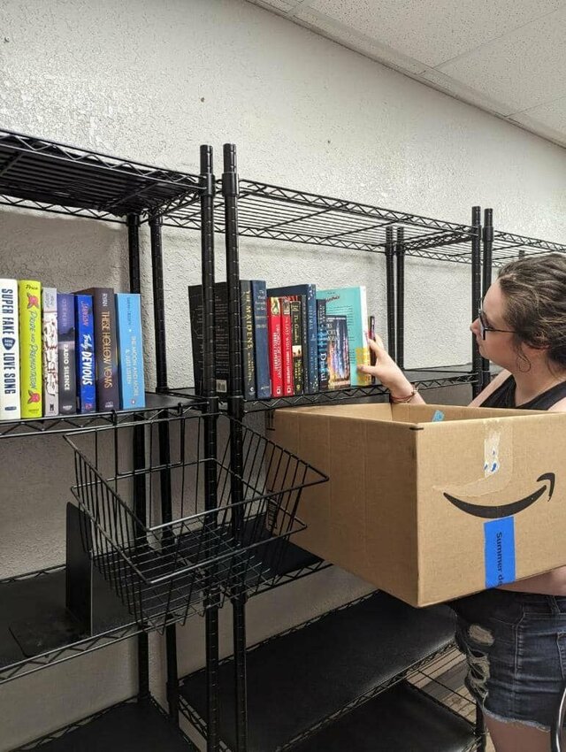 Rebekah Mauschbaugh, co-owner of Lamplight Bookstore, stocks the new business' shelves with used books in early July ahead of the grand opening later this month. The new bookstore is located in the back of Meyer's Market in downtown Warrensburg.   Photo courtesy of Lamplight Bookstore   &nbsp;