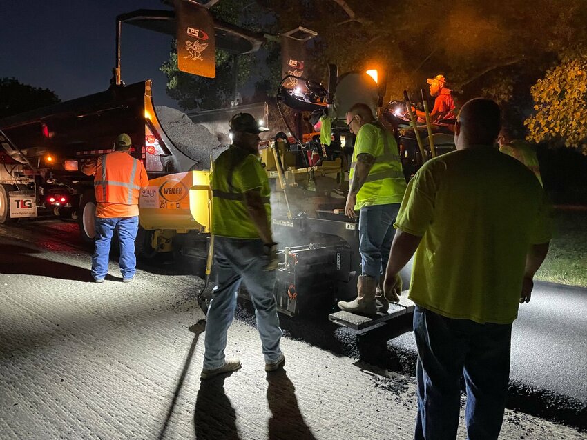 Sedalia Public Works Supervisor Justin Bray, in orange, helps the Sedalia street crew lay down a steaming bed of asphalt Monday night, Sept. 18 on Clinton Road. Work to the ditches should help preserve the new roadway.   Photo by Chris Howell | Democrat