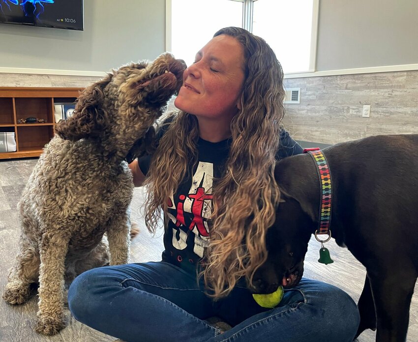 Valerie Henderson of the Hound Lounge, 711 W. Main St., gets some loving from kennel guest Tucker as her own pet, Archie, tries to get a friendly game of fetch going on Tuesday, Oct. 17. The new business opened last month.   Photo by Chris Howell | Democrat